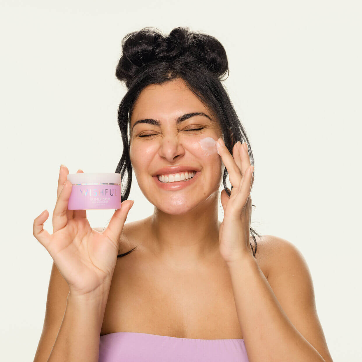 image showing happy girl using Huda Beauty Honey Balm Niacinamide Moisturizer available at heygirl.pk for delivery in Pakistan