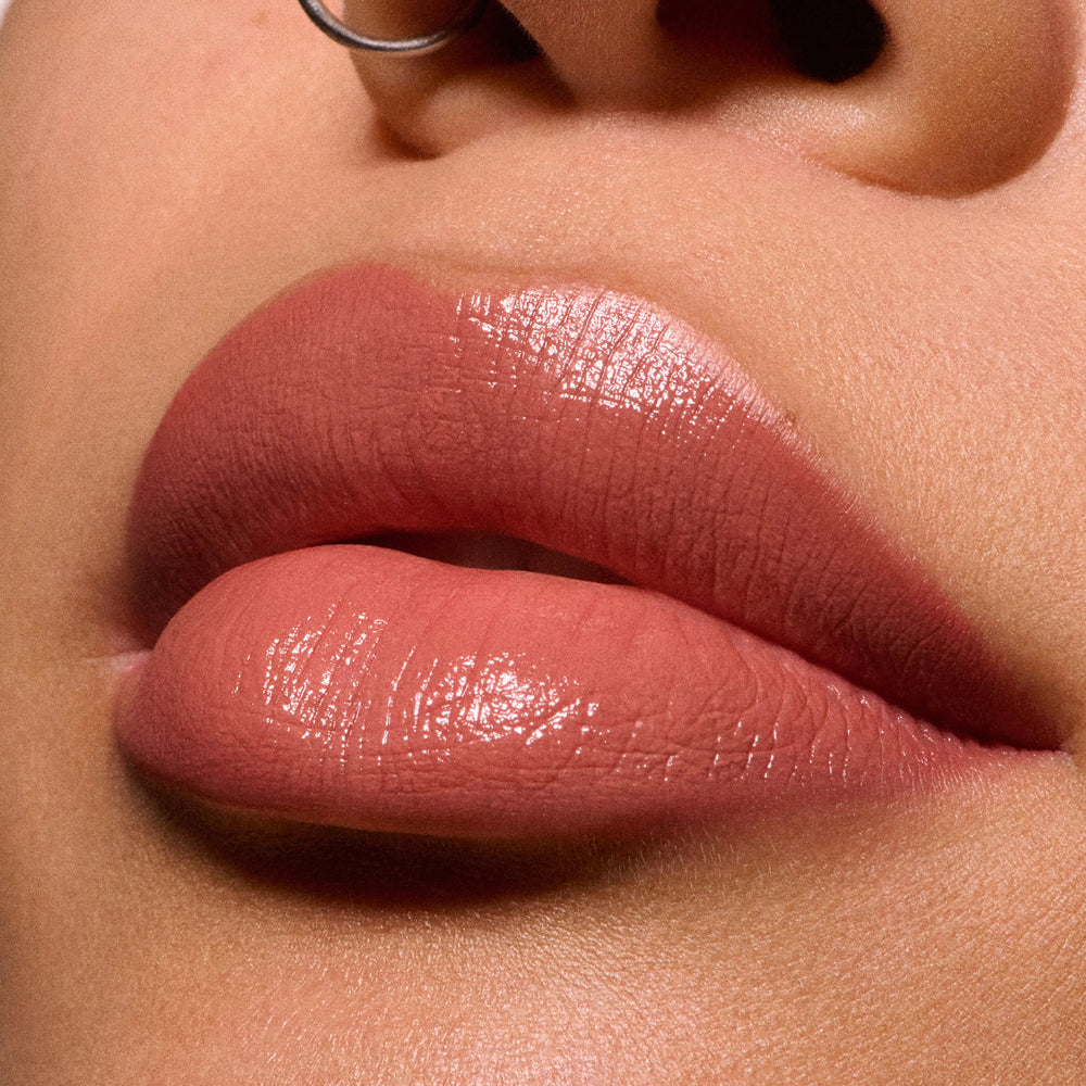 Close-up of MAC glossy nude pink lips with a metallic silver nose ring against warm skin tones.
