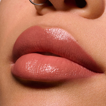 Close-up of MAC glossy nude pink lips with a metallic silver nose ring against warm skin tones.
