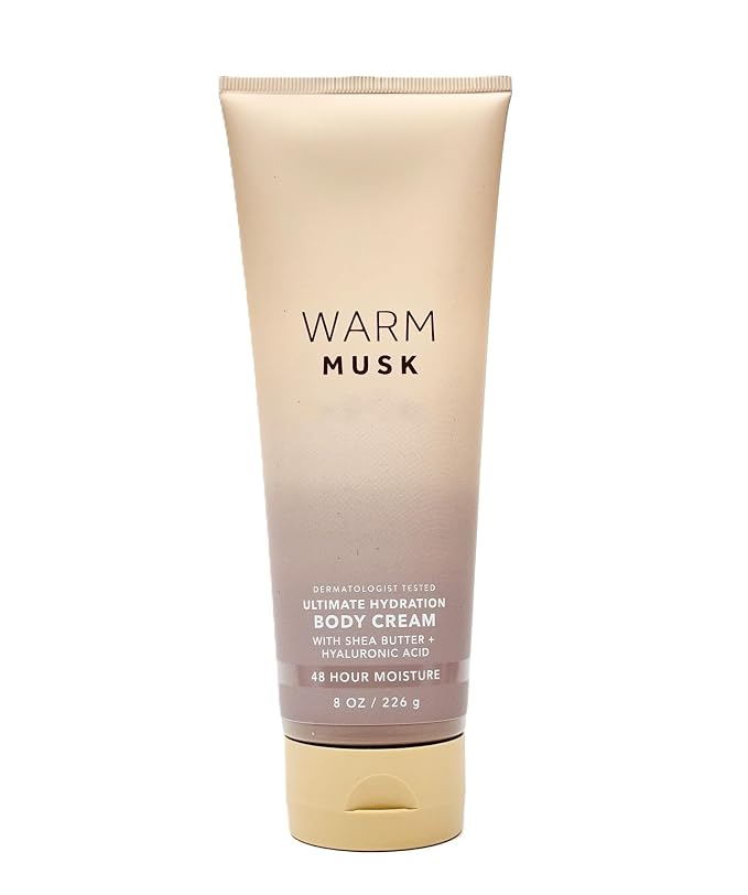 A squeeze tube of Warm Musk Ultimate Hydration Body Cream, featuring a beige-to-rose gold gradient design with a gold cap, set against a plain white background.