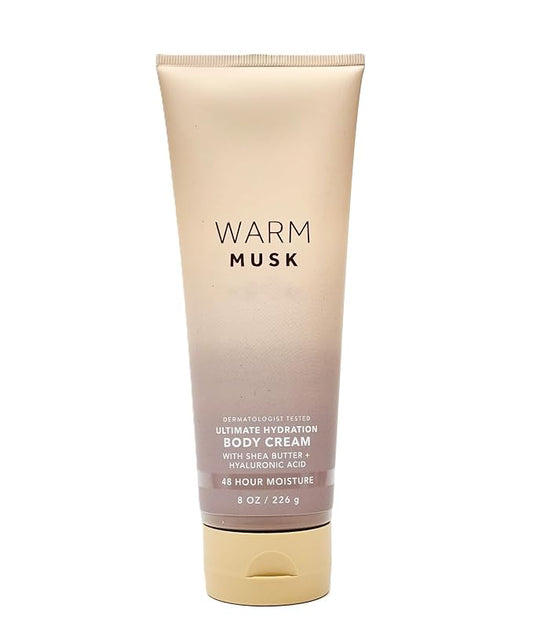 A squeeze tube of Warm Musk Ultimate Hydration Body Cream, featuring a beige-to-rose gold gradient design with a gold cap, set against a plain white background.