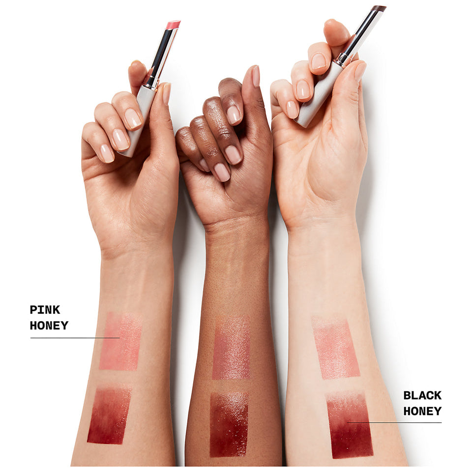 Three hands holding lipsticks with swatches on arms labeled 'Pink Honey' and 'Black Honey'.