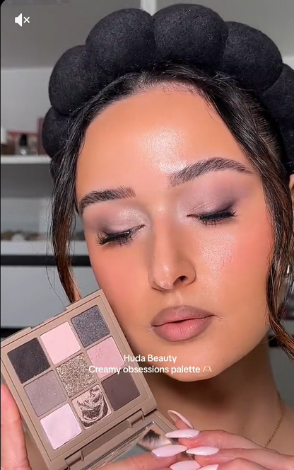 A Pakistani woman holding a Huda Beauty palette with makeup application on her face.