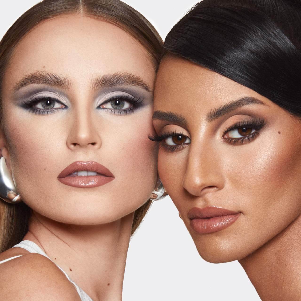 Two women with makeup close to each other on a plain background