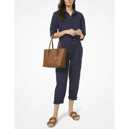A woman model carrying a brown Michael Kors leather tote bag and brown slide sandals against a plain white studio background.