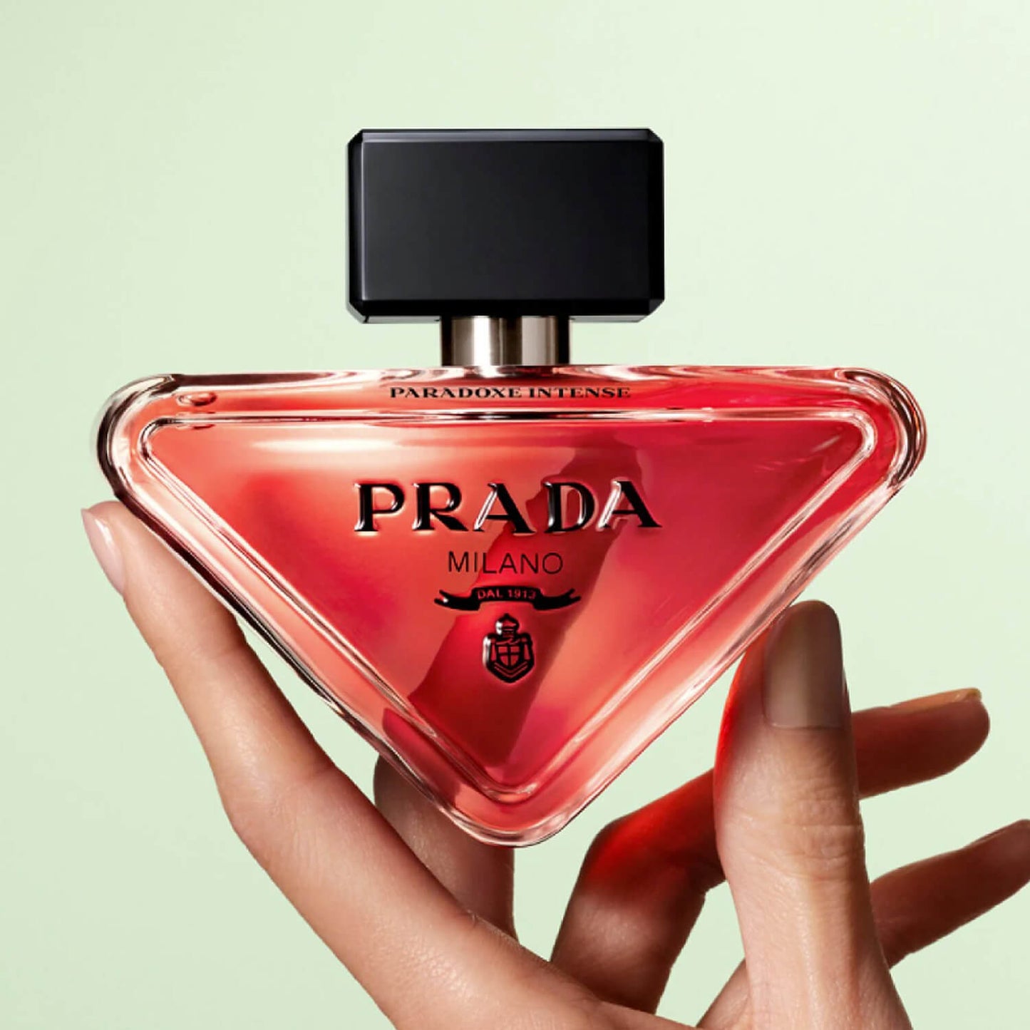 Prada perfume bottle held by a hand against a light green background