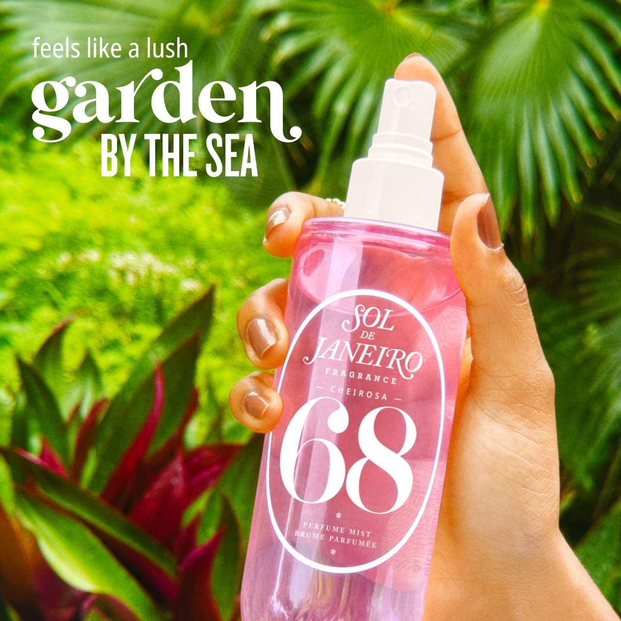 Hand holding a pink perfume spray bottle with green foliage in the background
