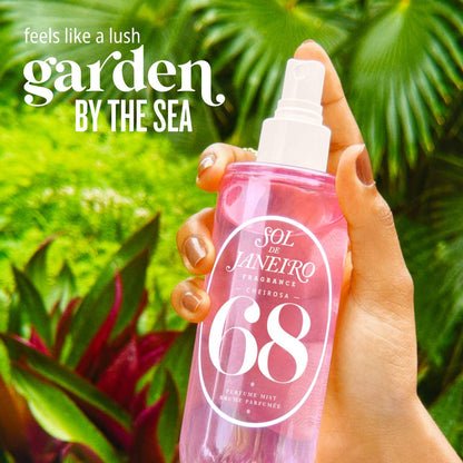 Hand holding a pink perfume spray bottle with green foliage in the background