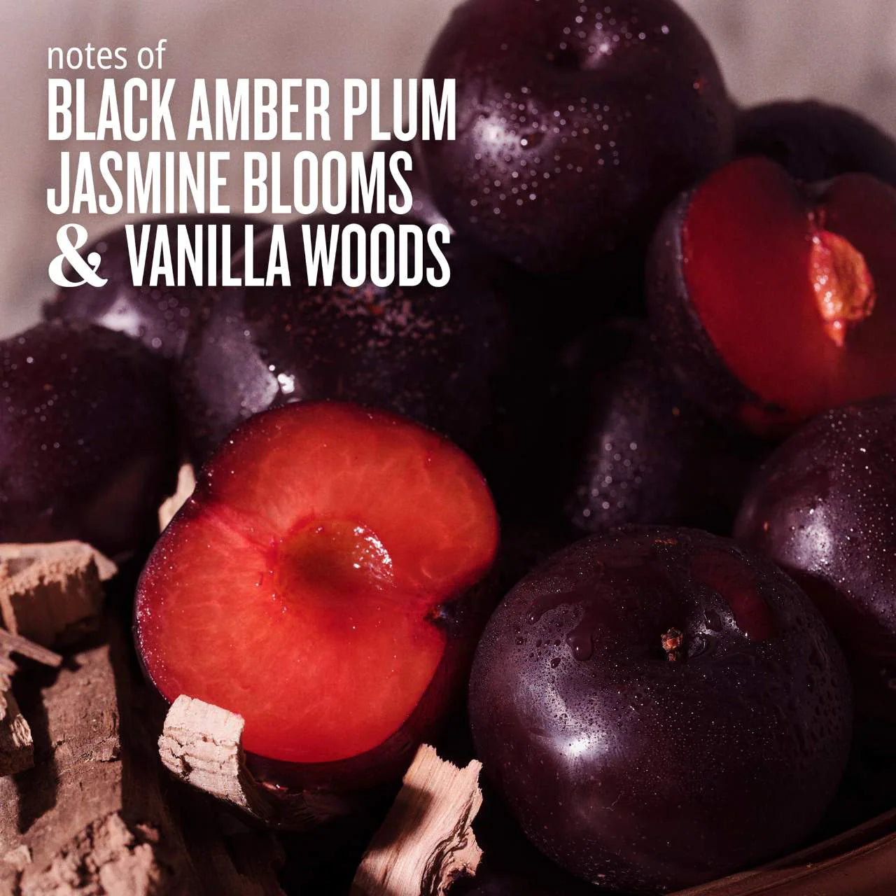 Close-up of black amber plums with text 'notes of Black Amber Plum, Jasmine Blooms & Vanilla Woods' on a textured background.